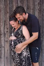 Werdende Eltern halten sich liebevoll vor einer Holzwand